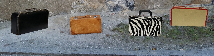 vier kunstvoll platzierte Koffer vor alter Hauswand